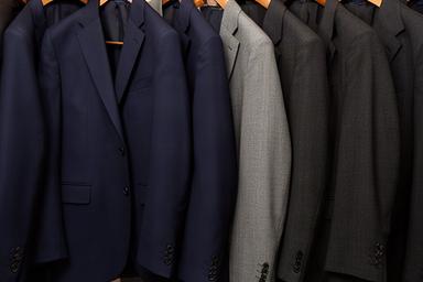 Navy and charcoal business suits on wooden hangers against a neutral backdrop in a menswear shop
